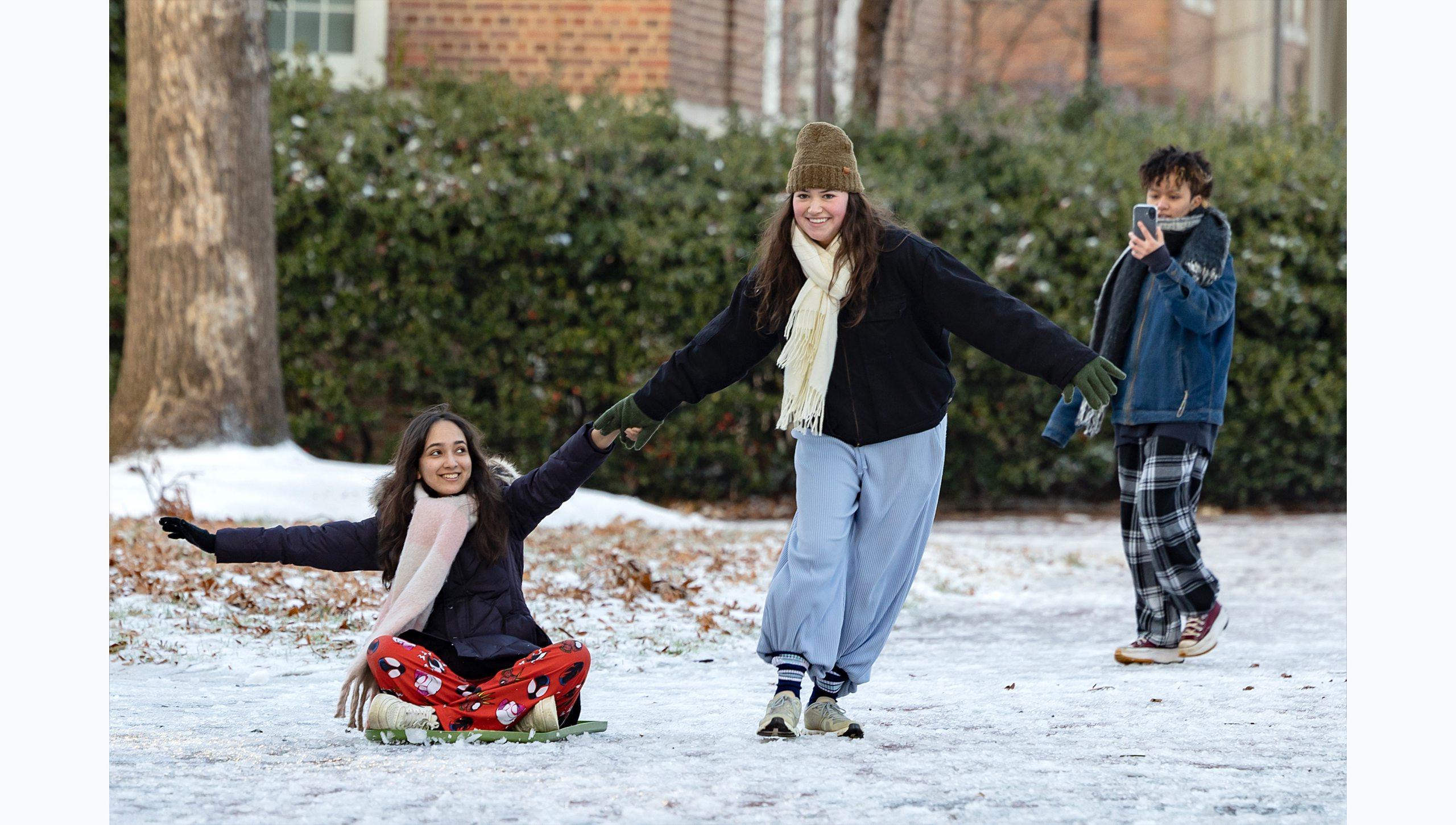 One student pulling another on a sled on the snowy campus of U.N.C Chapel Hill.